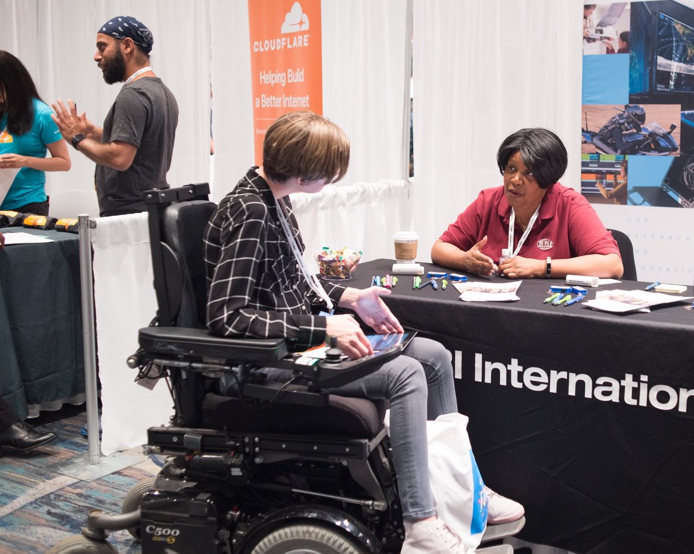 Tapia 2019 conference attendee in wheelchair speaking with conference recruiter who is seated at a table